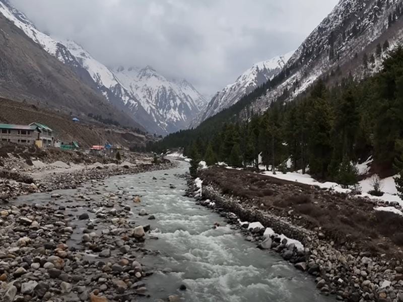 Scenic Baspa River flowing through Himalayas, surrounded by lush greenery & snow-capped peaks